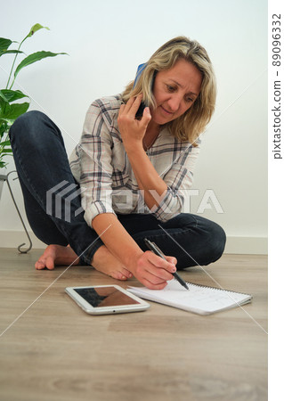the girl is sitting on the floor with a phone and a notebook the girl is sitting on the floor with a phone and a notebook 89096332
