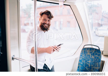 Young bearded man with smartphone smiling in train 89096831