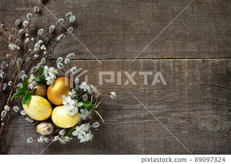 Golden Colored easter eggs in a nest with willow branches and spring flowers on a gray wooden background. Top view flat lay background. Copy spa 89097824
