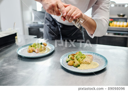 Close-up of chef adding spices from shaker on ready dishes on table before serving Close-up of chef adding spices from shaker on ready dishes on table before serving 89098096