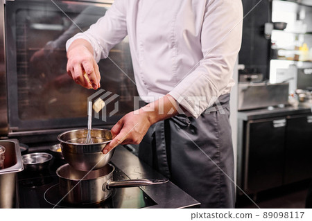 Close-up of chef in apron throwing butter in bowl and melting it on cooker to prepare a dessert 89098117
