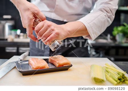 Close-up of chef adding spices on fish meat before cooking japanese dish at table in kitchen 89098120