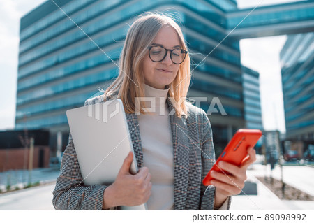 Portrait of successful blond hair woman using smartphone, holding digital tablet in urban building background. Business people concept 89098992