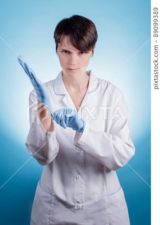 Female doctor in white coat putting on blue gloves on hands. Healthcare And Medical concept. Female doctor in white coat putting on blue gloves on hands. Healthcare And Medical concept. 89099389