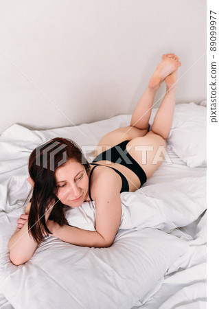 Portrait of a young beautiful brunette lying in bed wearing underwear 89099977