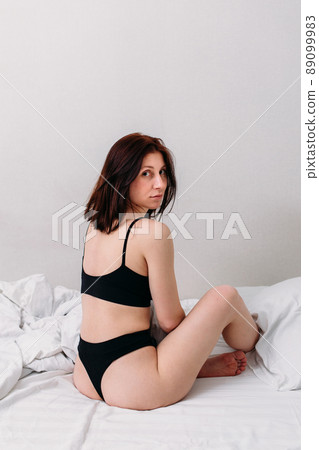 Portrait of a young beautiful brunette lying in bed wearing underwear 89099983