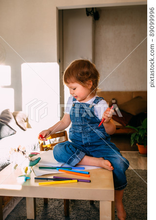 Small child at home at the children's table draws with felt-tip pens. 89099996