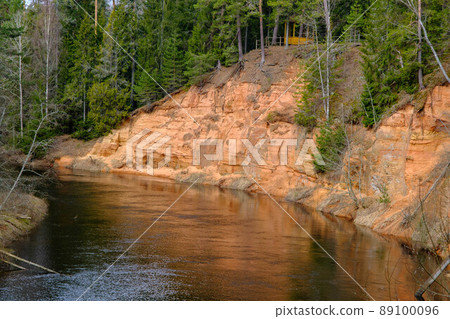 The Echo cliff near river Salaca in Mazsalaca nature park. Beautiful natural formation. A naturally formed cave in the sandstone rock. A river flows along the cave. Devonian period. 89100096