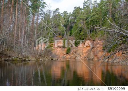 The Echo cliff near river Salaca in Mazsalaca nature park. Beautiful natural formation. A naturally formed cave in the sandstone rock. A river flows along the cave. Devonian period. The Echo cliff near river Salaca in Mazsalaca nature park. Beautiful natural formation. A naturally formed cave in the sandstone rock. A river flows along the cave. Devonian period. 89100099