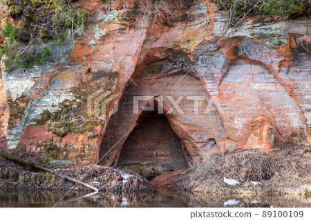 View to the Angels cave, a red sandstone cliff at the river Salaca in Skanaiskalns Nature Park in Mazsalaca in April in Latvia. View to the Angels cave, a red sandstone cliff at the river Salaca in Skanaiskalns Nature Park in Mazsalaca in April in Latvia. 89100109