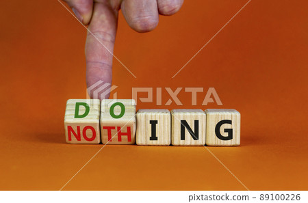 Doing or nothing symbol. Businessman turns wooden cubes and changes the word Nothing to Doing. Beautiful orange background, copy space. Business, doing or nothing concept. 89100226