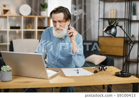 Portrait of handsome elegant mature business man with cigar sitting at desk with laptop Portrait of handsome elegant mature business man with cigar sitting at desk with laptop 89100413