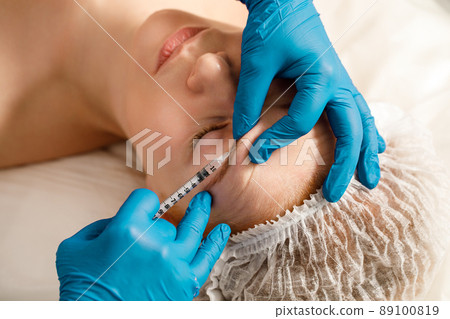 A cosmetologist performs a procedure of rejuvenating injections for the face to tighten and smooth out wrinkles on the skin of a woman's face. Cosmetic skin care in a beauty salon. A cosmetologist performs a procedure of rejuvenating injections for the face to tighten and smooth out wrinkles on the skin of a woman's face. Cosmetic skin care in a beauty salon. 89100819