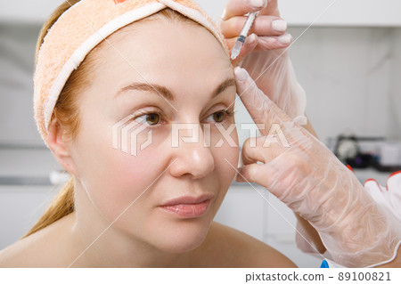 A cosmetologist performs a procedure of rejuvenating injections for the face to tighten and smooth out wrinkles on the skin of a woman's face. Cosmetic skin care in a beauty salon. A cosmetologist performs a procedure of rejuvenating injections for the face to tighten and smooth out wrinkles on the skin of a woman's face. Cosmetic skin care in a beauty salon. 89100821