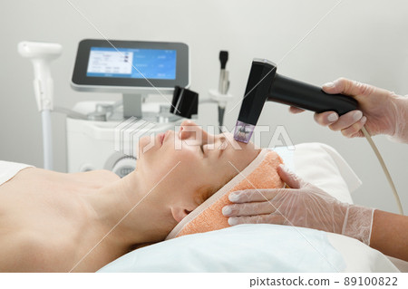 A woman receives laser treatment of the face in a cosmetology clinic, a concept of skin rejuvenation is being developed. laser peeling A woman receives laser treatment of the face in a cosmetology clinic, a concept of skin rejuvenation is being developed. laser peeling 89100822