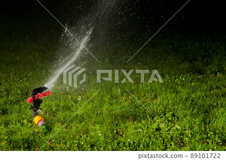 lawn sprinkler spraying water over green grass at night 89101722