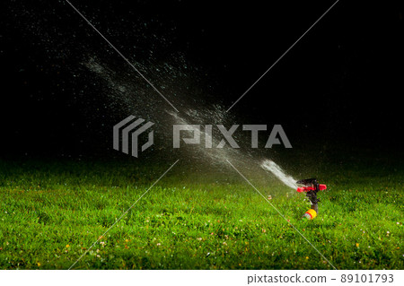 lawn sprinkler spraying water over green grass at night 89101793