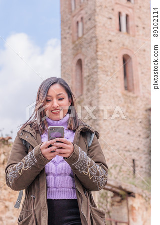 Latin Honduran young woman texting in cellular chat during travel in Buitrago de Lozoya, Spain Latin Honduran young woman texting in cellular chat during travel in Buitrago de Lozoya, Spain 89102114