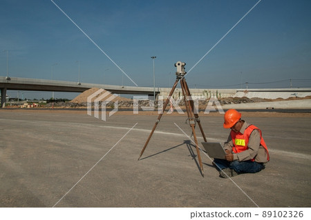 Engineer or surveyor working with theodolite equipment at road construction site. 89102326