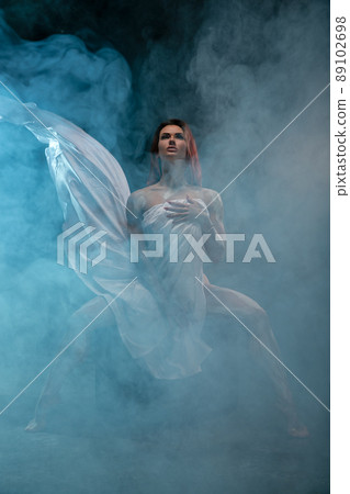 Red-haired girl covers herself with white cloth like an antique statue, posing in the studio Red-haired girl covers herself with white cloth like an antique statue, posing in the studio 89102698