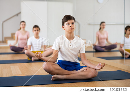 Boy sitting in lotus pose while exercising yoga with family in fitness center Boy sitting in lotus pose while exercising yoga with family in fitness center 89105883