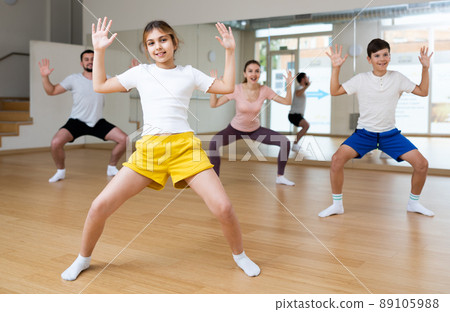 Girl practising dance moves with parents and sibling indoors 89105988