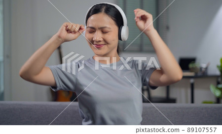Happy woman with headphones and listening to music sitting on sofa at home. Happy woman with headphones and listening to music sitting on sofa at home. 89107557