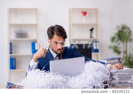 Young male employee and a lot of cut papers in the office 89109131