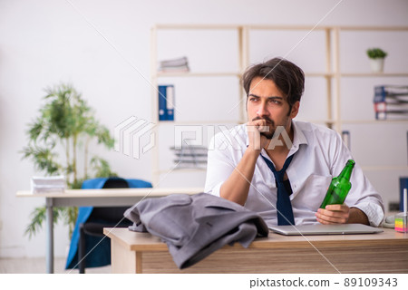 Young alcohol addicted employee sitting in the office Young alcohol addicted employee sitting in the office 89109343