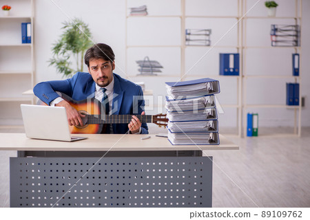 Young male employee playing guitar at workplace 89109762
