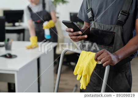 Hands of African American male cleaner choosing music in smartphone Hands of African American male cleaner choosing music in smartphone 89109819