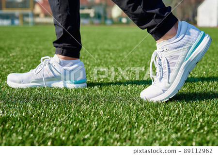Male runner feet with white sneakers at stadium with green grass, close up. Sport sneakers for jogging. Fitness and healthy lifestyle concept Male runner feet with white sneakers at stadium with green grass, close up. Sport sneakers for jogging. Fitness and healthy lifestyle concept 89112962