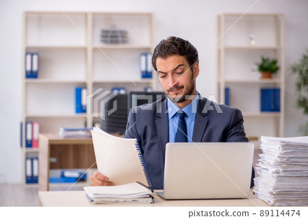 Young male employee and too much work in the office Young male employee and too much work in the office 89114474