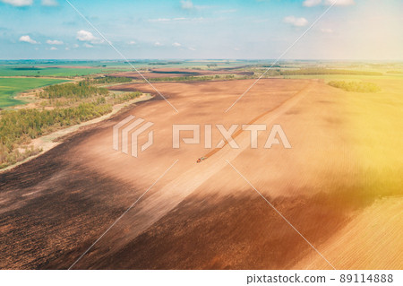 Aerial view, Top View Tractor Plowing Field In Spring Season. Beginning Of Agricultural Spring Season. Cultivator Pulled By A Tractor In Countryside Rural Field Landscape 89114888