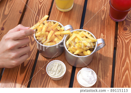 Man's hand holding french fries. Top view of table with lemonades, fast food, sauces, french fries. Man's hand holding french fries. Top view of table with lemonades, fast food, sauces, french fries. 89115113