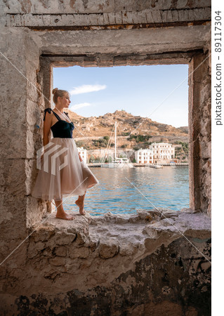 Side view portrait of a relaxed woman breathing fresh air at the seaside. She stands on the window in the old building. Side view portrait of a relaxed woman breathing fresh air at the seaside. She stands on the window in the old building. 89117304