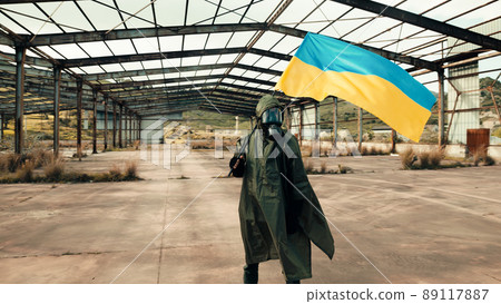 Soldier man with gas mask waves Ukrainian flag in a war warehouse 89117887