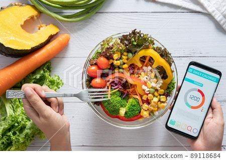 Calories counting , diet , food control and weight loss concept. Calorie counter application on smartphone screen at dining table with salad, fruit juice, bread and fresh vegetable. healthy eating 89118684