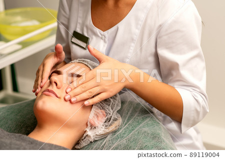 Face massage. Beautiful caucasian young white woman having a facial massage with closed eyes in a spa salon Face massage. Beautiful caucasian young white woman having a facial massage with closed eyes in a spa salon 89119004