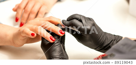 The manicurist finishes the procedure for red nail polishing and cleaning with a cotton napkin, pad, swab in a beauty salon, close up The manicurist finishes the procedure for red nail polishing and cleaning with a cotton napkin, pad, swab in a beauty salon, close up 89119043