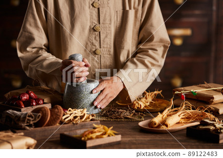 Front view of apocathery putting ingredient into mortar and pestle with chinese traditional medicine in wooden table  89122483