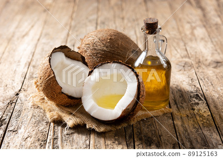sliced coconuts with oil inside and bottle of coconut oil on wooden table 89125163
