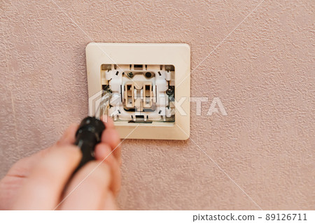 a man repairs an electrical outlet. electrician and handyman services. a man repairs an electrical outlet. electrician and handyman services. 89126711