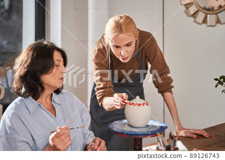 Skilful designer advising to her senior student while working at the pottery master class Skilful designer advising to her senior student while working at the pottery master class 89126743