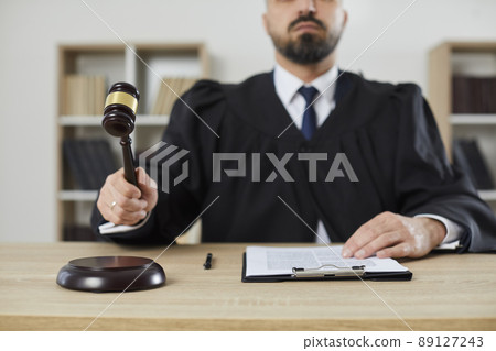 Male judge who passes sentence and announces closure of case by hitting gavel on sounding block. Male judge who passes sentence and announces closure of case by hitting gavel on sounding block. 89127243