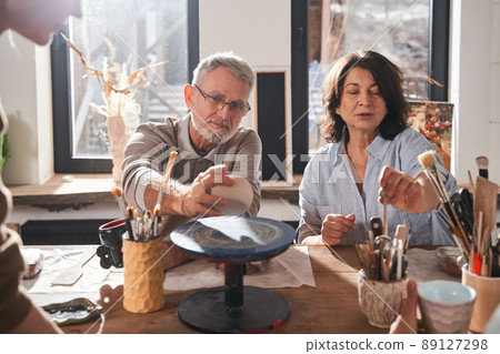 Two mature people examining equipment at the pottery master class while sitting 89127298