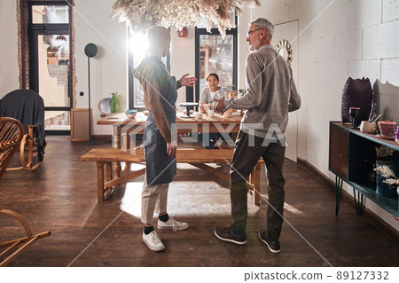 Woman talking with senior man while greeting him at the pottery art school Woman talking with senior man while greeting him at the pottery art school 89127332