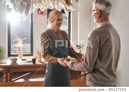 Woman holding senior man at the hands while greeting him at the pottery art school Woman holding senior man at the hands while greeting him at the pottery art school 89127333