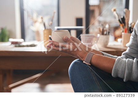 Senior woman holding fresh cup from clay at her hands while chatting with female artist 89127339