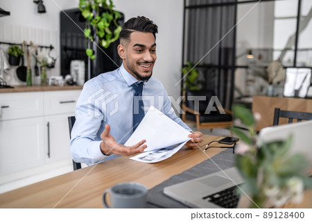 A dark-haired businessman having online meeting at his home office A dark-haired businessman having online meeting at his home office 89128400